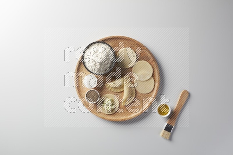 two closed sambosas and one open sambosa filled with cheese while flour, salt, black pepper and oil with oil brush aside in a wooden dish on a white background
