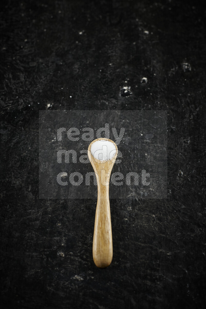 A wooden spoon full of white salt on black background