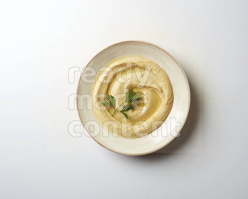 Hummus in a pottry plate garnished with parsley on a white back ground