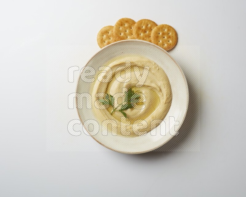 Hummus in a pottry plate garnished with parsley on a white back ground