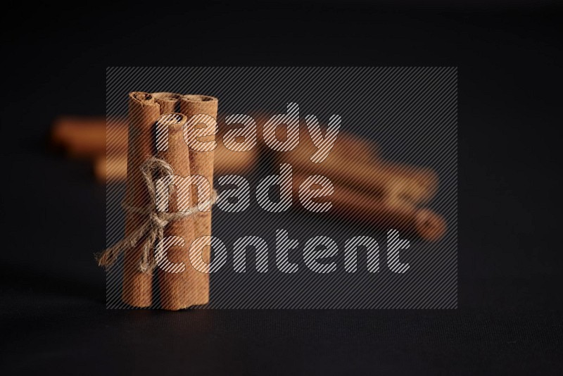 4 Cinnamon sticks stacked and bounded with more sticks in the background on black flooring