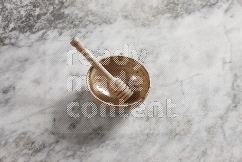 Beige pottery bowl with wooden honey dipper in it on grey marble background