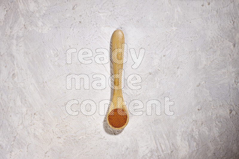 A wooden spoon full of ground paprika powder on white background