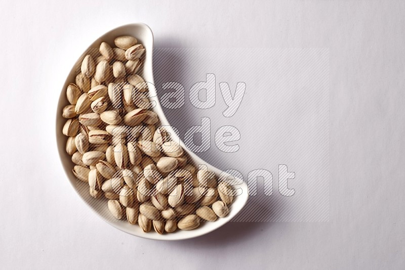 Pistachios in a crescent pottery plate on white background