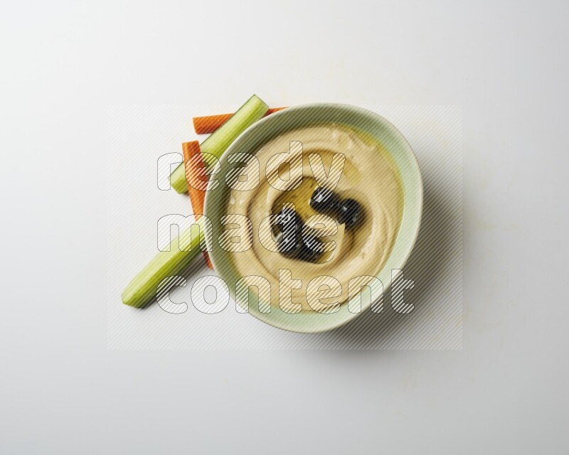 Hummus in a green plate garnished with black olives on a white background
