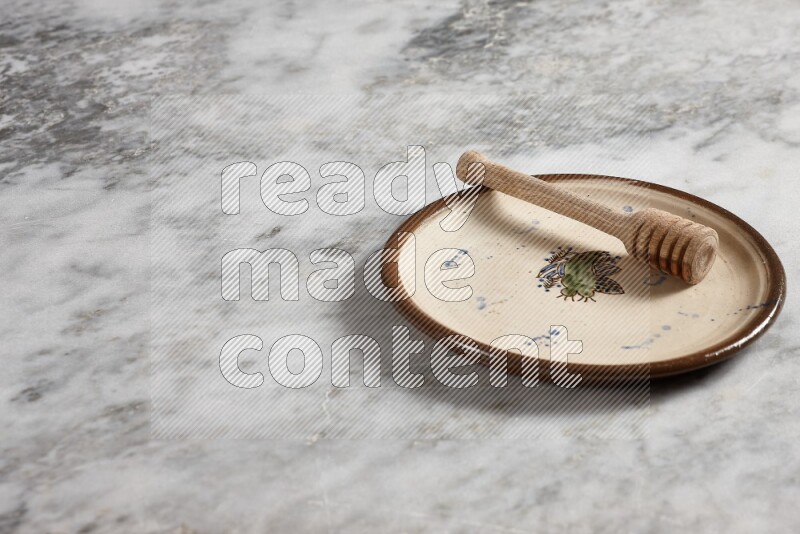 Decorative pottery plate with wooden honey dipper in it on grey marble background