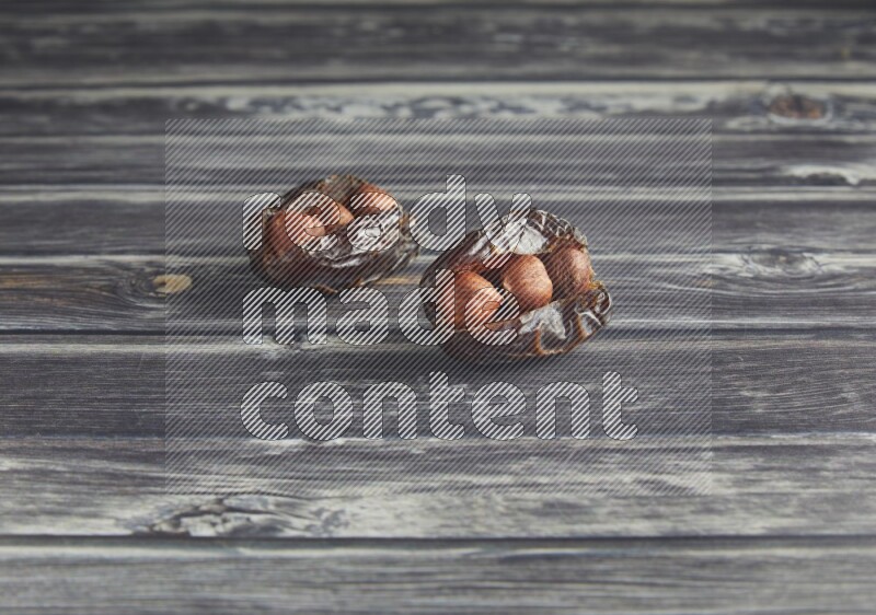 two hazelnut stuffed madjoul dates on a wooden grey background