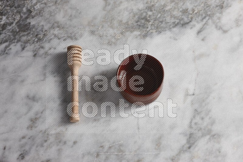 Brown pottery bowl with wooden honey dipper on the side on grey marble background