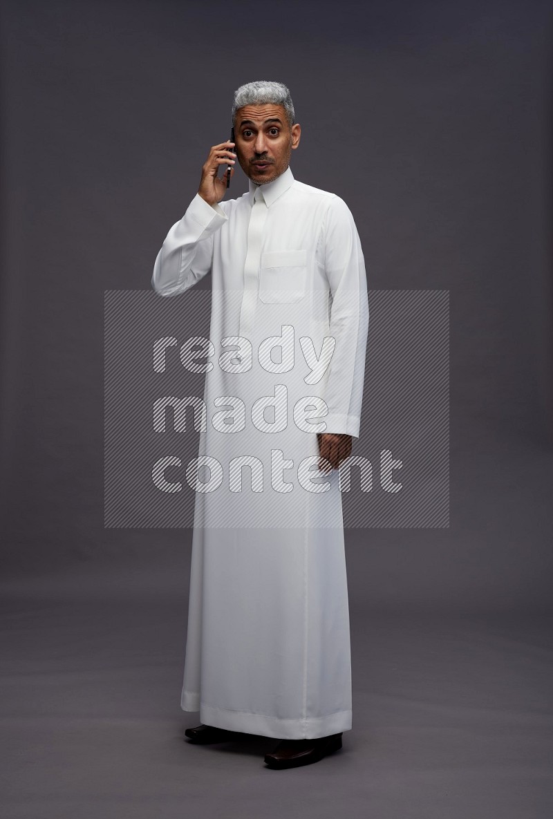 Saudi man wearing thob standing talking on phone on gray background