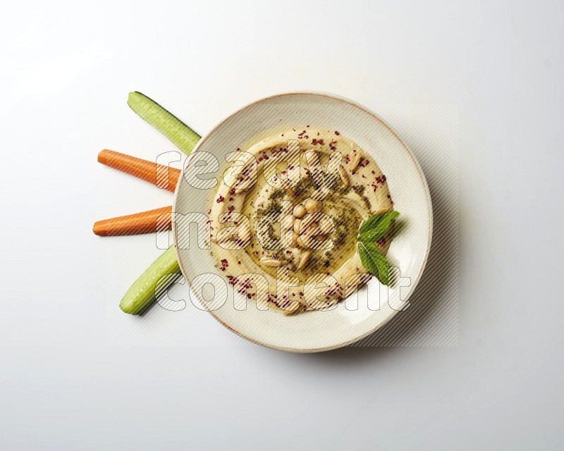 Hummus in a pottry plate garnished with zaatr & sumak on a white background