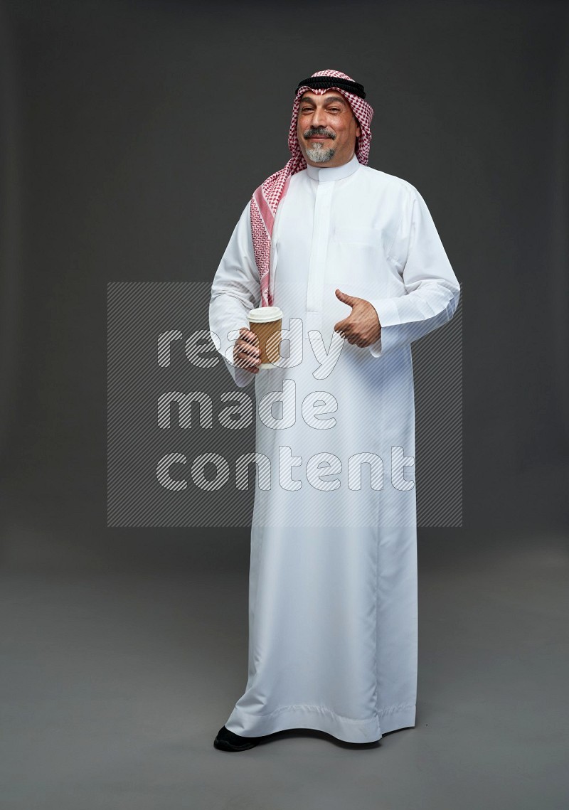 Saudi man with shomag Standing holding paper cup on gray background