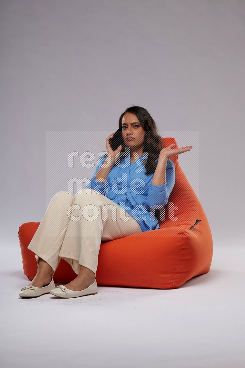 A woman sitting on an orange beanbag and talking on the phone