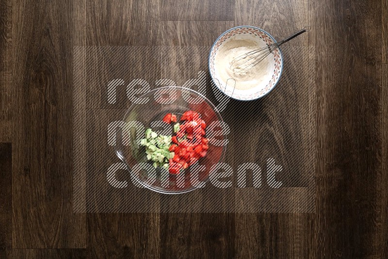 A bowl full of salad (avocado, tomatoes, red beans, olives, bell pepper, corn, lettuce) and bowl of salad dressing on wooden background