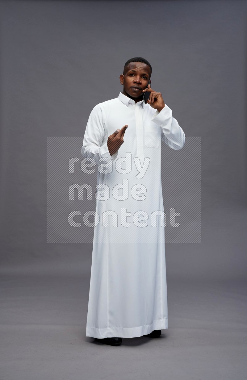 Saudi man wearing thob standing talking on phone on gray background