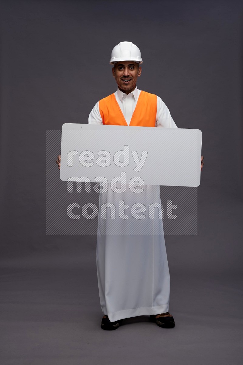 Saudi man wearing thob with engineer vest standing holding board on gray background