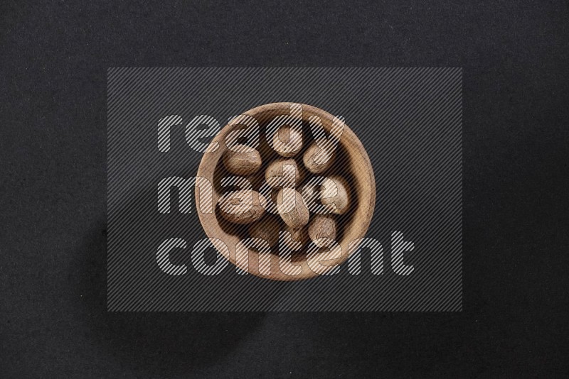 A wooden bowl full of nutmeg on a black flooring in different angles