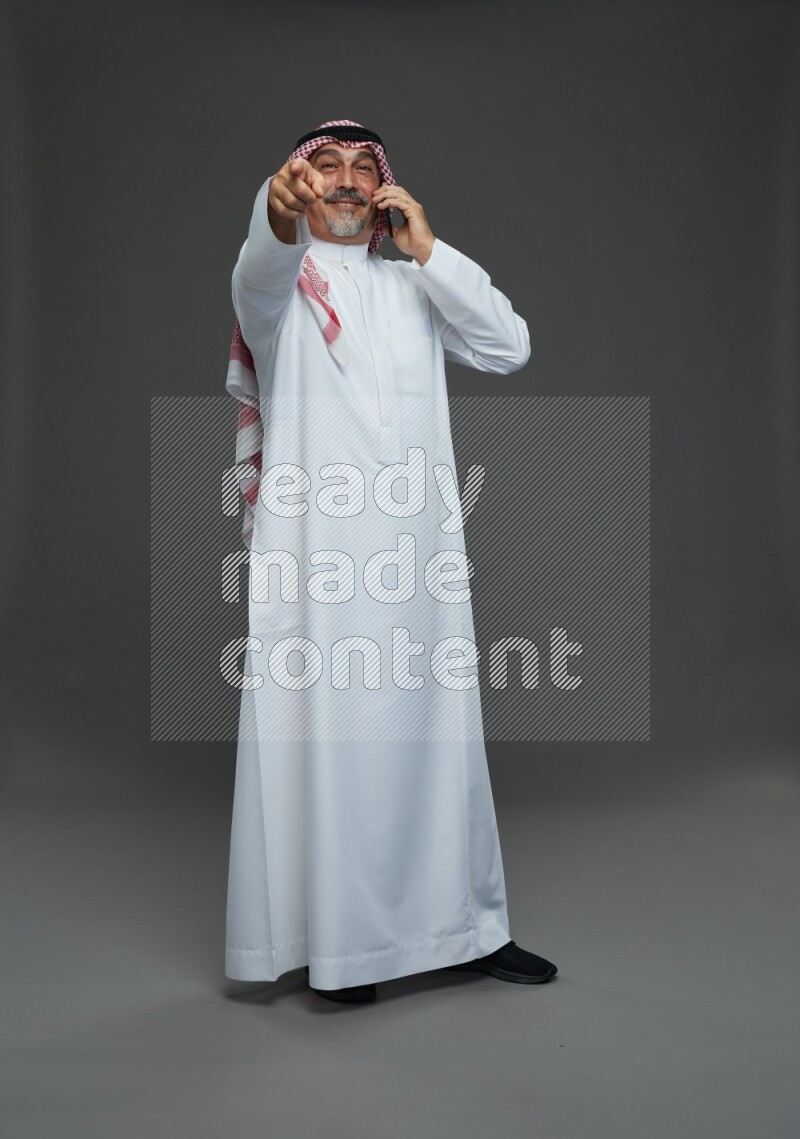 Saudi man with shomag Standing talking on phone on gray background