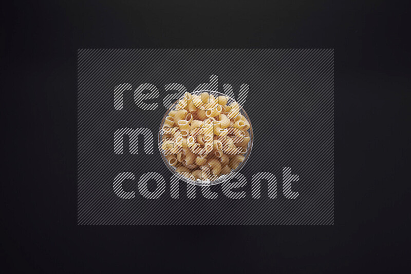Elbow pasta in a glass bowl on black background