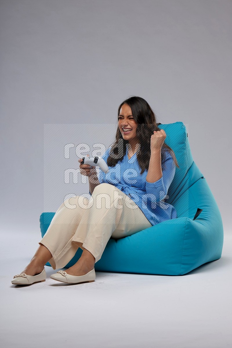 A woman sitting on a blue beanbag and gaming with joystick