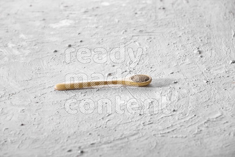 A wooden spoon full of black pepper powder on a textured white flooring