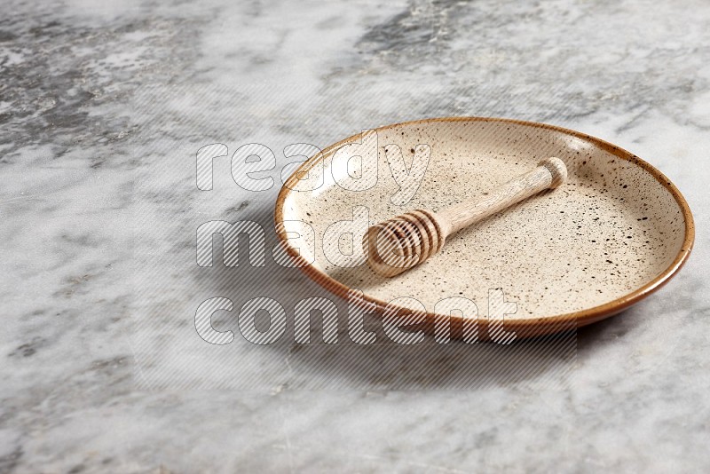 Beige Pottery Plate with wooden honey handle in it, on grey marble flooring, 45 degree angle