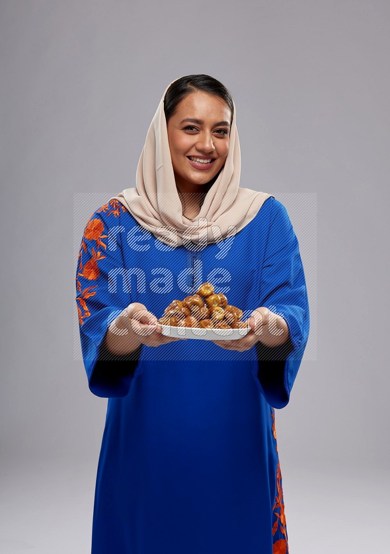 A Saudi woman standing wearing Jalabeya holding a plate of dates