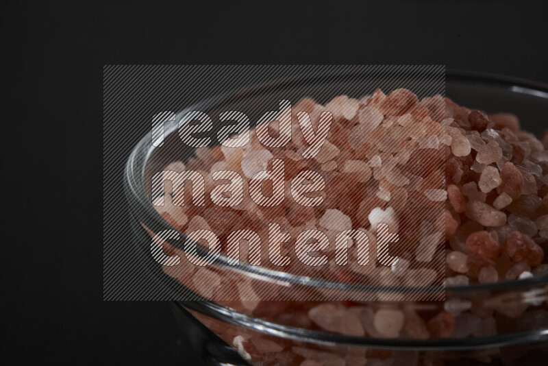 A glass bowl full of coarse himalayan salt crystals on black background