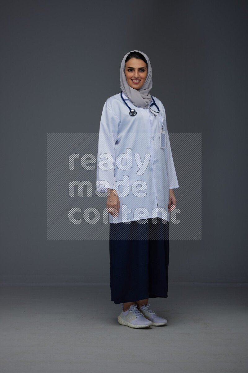 A female doctor wearing a light gray head scarf standing on grey background.