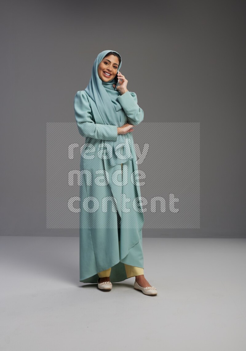 Saudi Woman wearing Abaya standing talking on phone on Gray background