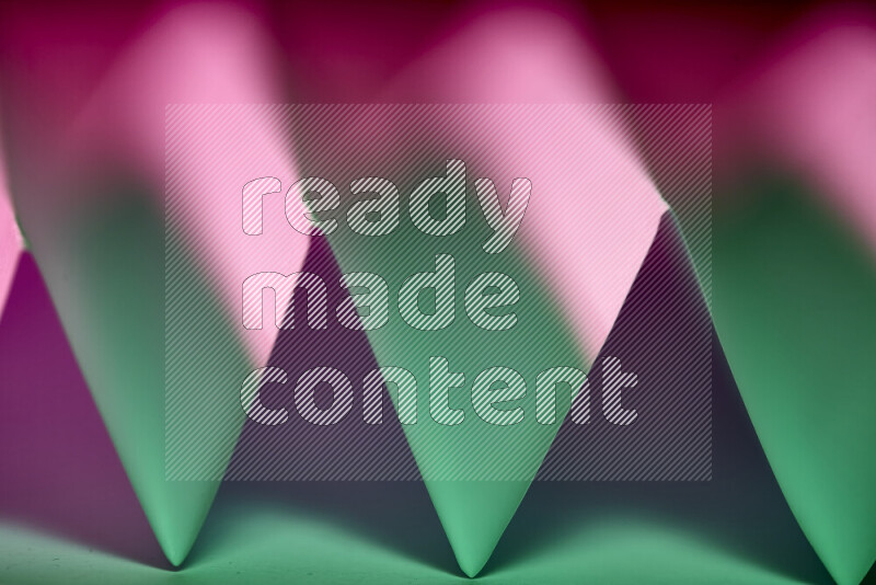 A close-up abstract image showing sharp geometric paper folds in green and purple gradients