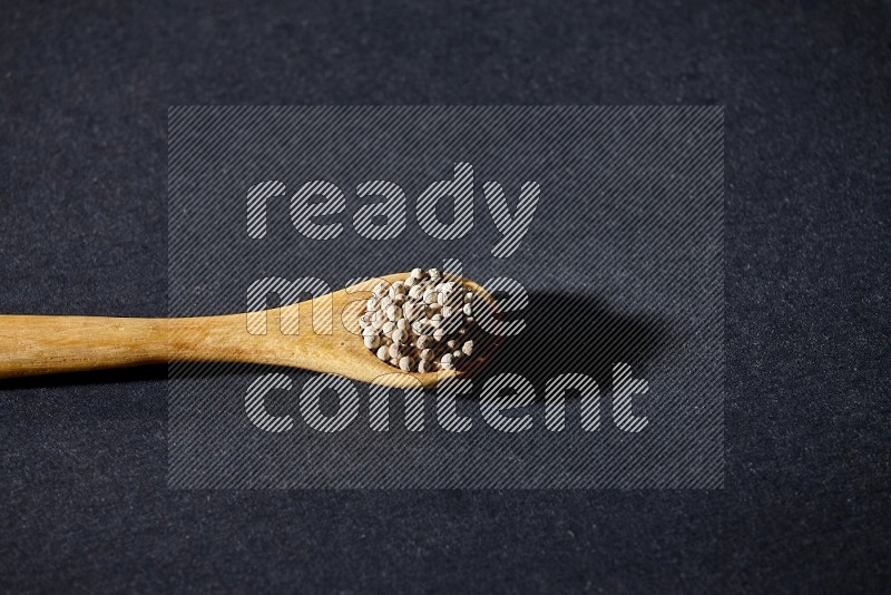 A wooden spoon full of white pepper beads on black flooring