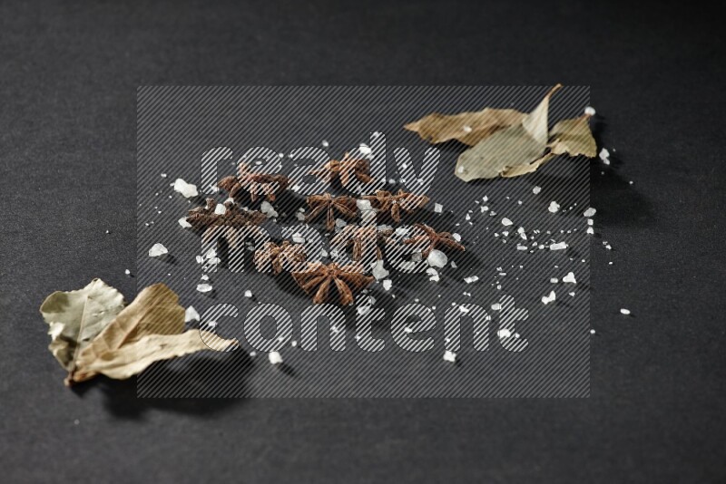 Salt, star anise and bay laurel on black flooring