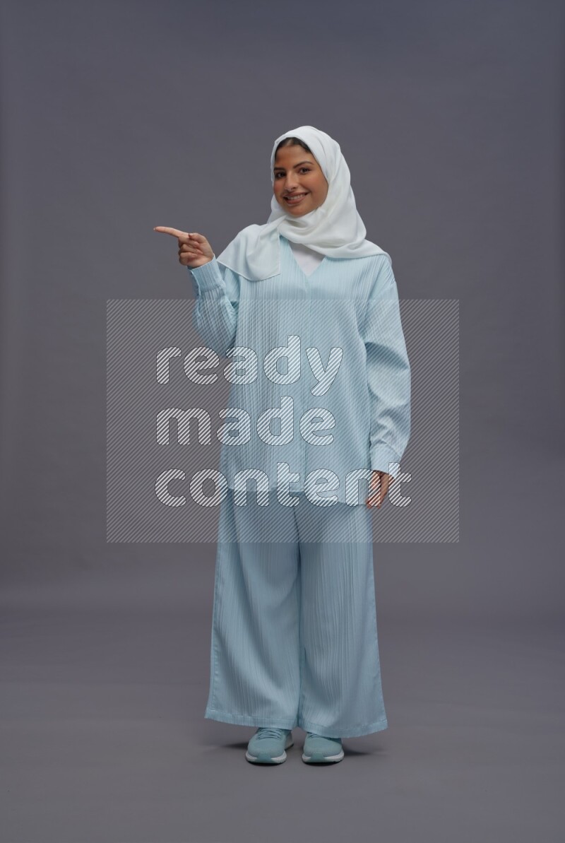 Saudi woman wearing hijab clothes standing interacting with the camera on gray background
