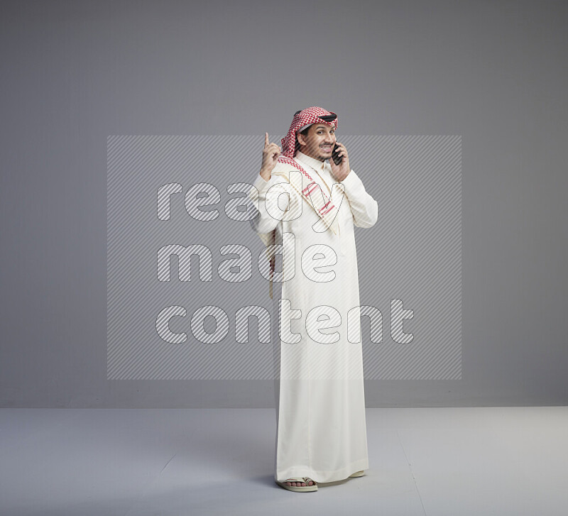 رجل سعودي يرتدي ثوب ابيض وشماغ احمر يتحدث في الجوال
