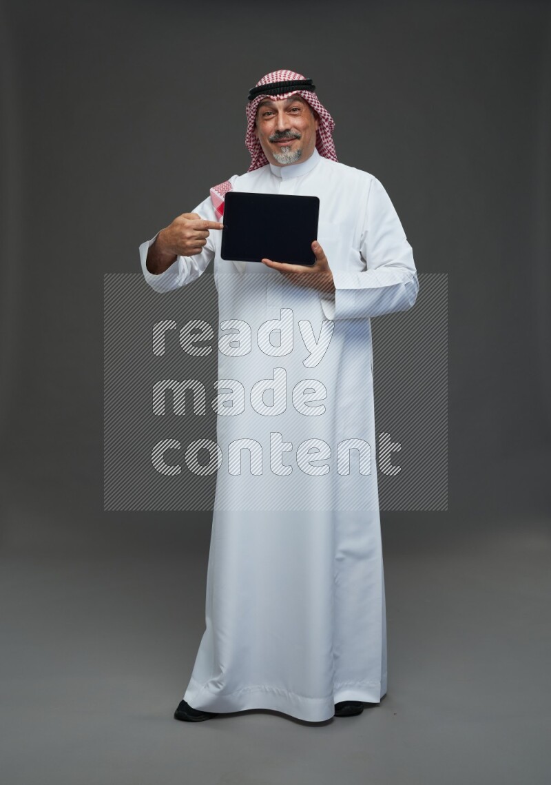 Saudi man with shomag Standing working on tablet on gray background