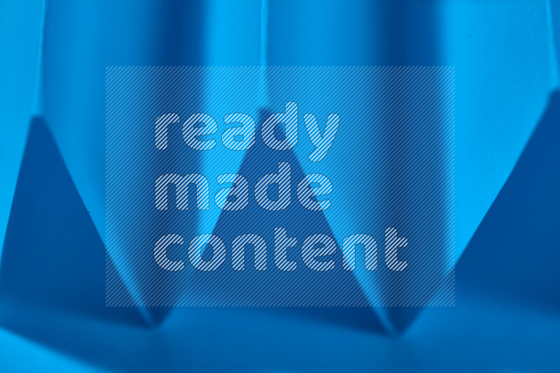 A close-up abstract image showing sharp geometric paper folds in blue gradients