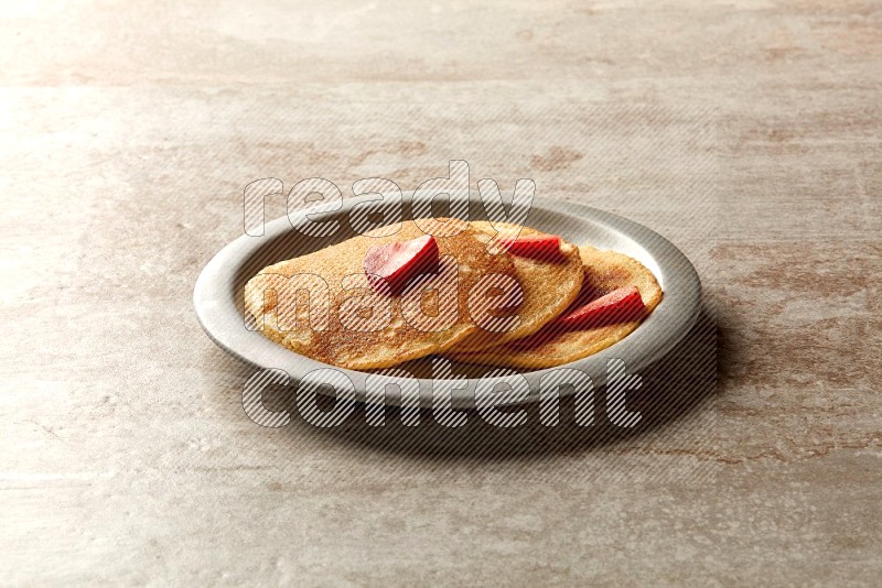 Three stacked strawberry pancakes in a grey plate on beige background