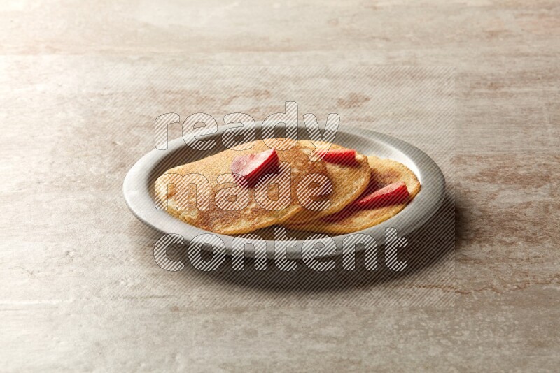 Three stacked strawberry pancakes in a grey plate on beige background