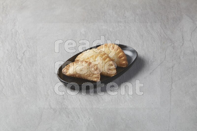 Four fried sambosas in an oval shaped black plate on a gray background