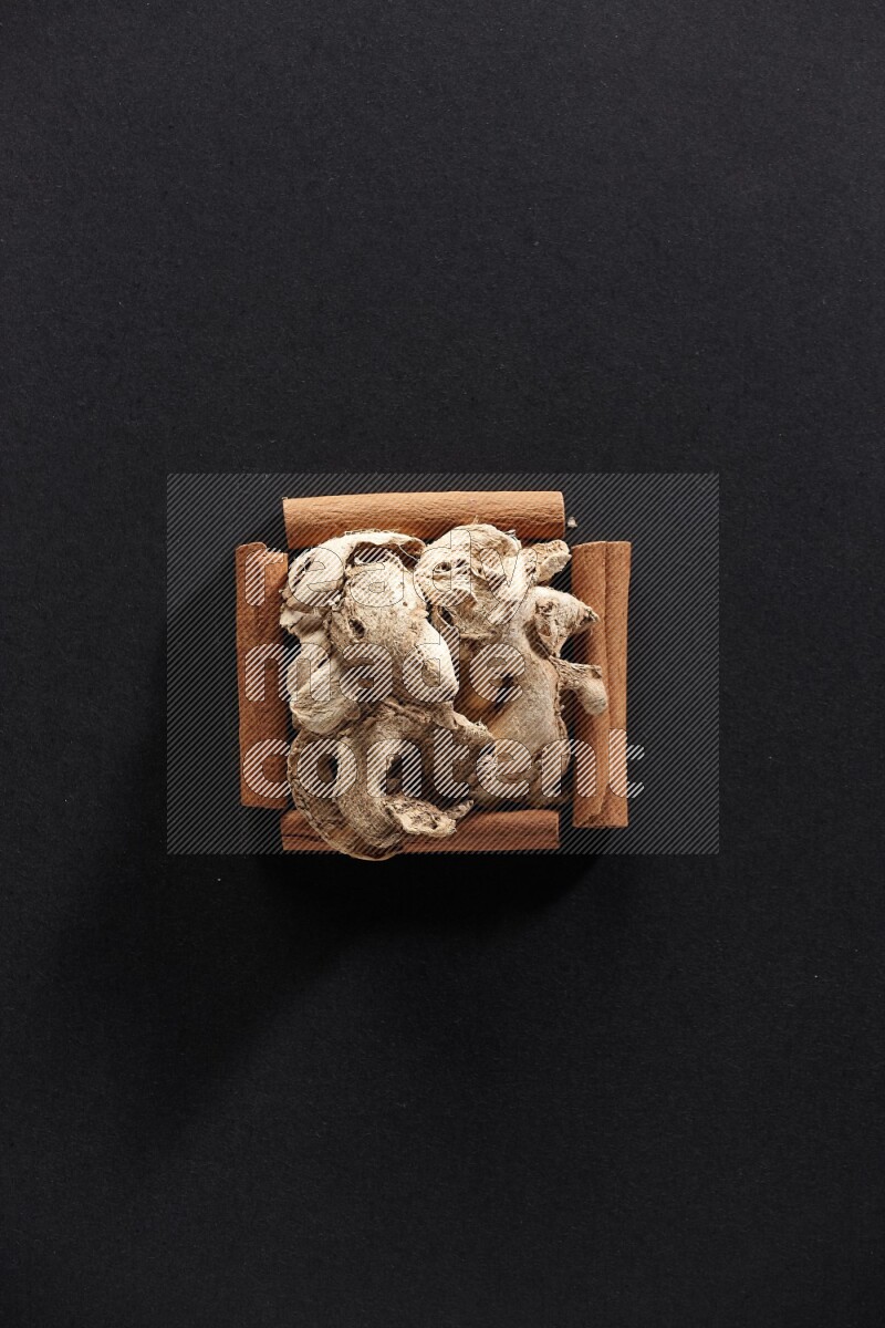 A single square of cinnamon sticks full of dried ginger on black flooring