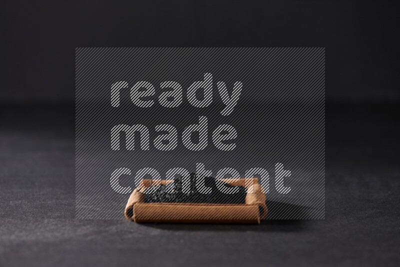 A single square of cinnamon sticks full of black seeds on black flooring