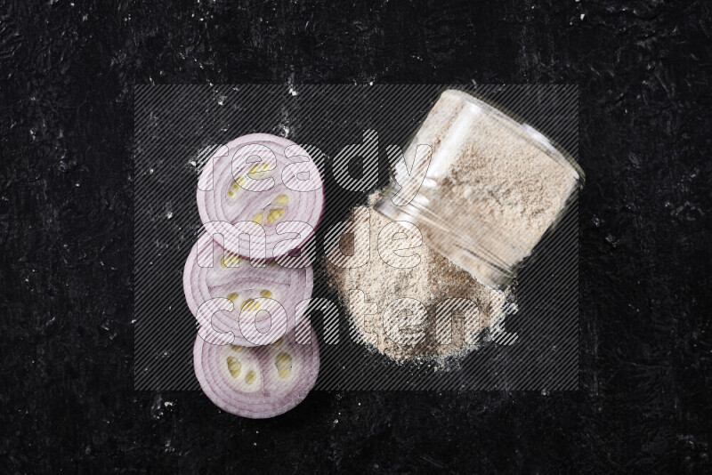 A glass jar full of onion powder flipped with some spilling powder on black background