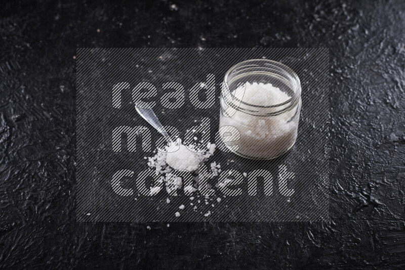 A glass jar full of coarse sea salt crystals on black background