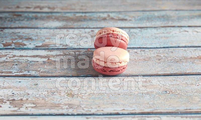 45º Shot of two Pink Litchi Raspberry macarons on light blue wooden background