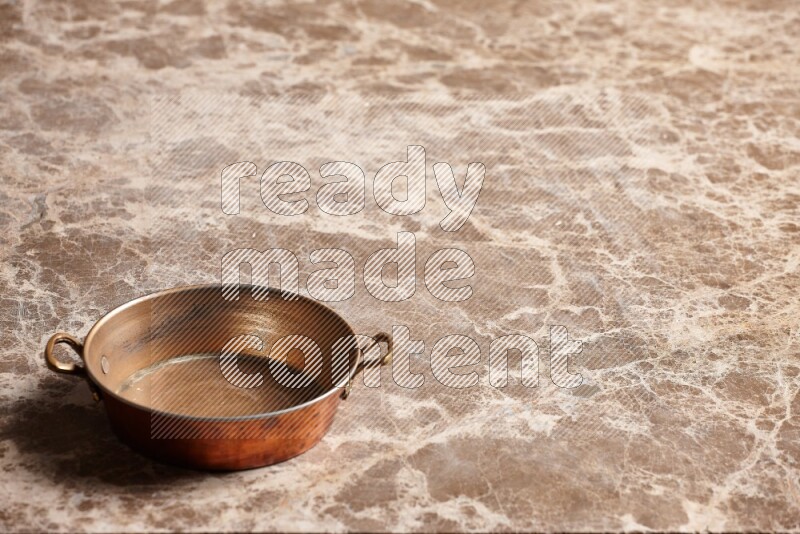 A small copper pan on beige marble background