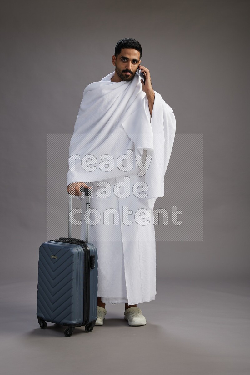 A man wearing Ehram Standing holding traveling bag on gray background