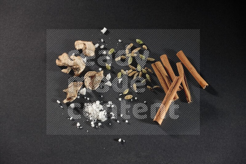 Ginger, salt, cardamom and cinnamon sticks on black flooring