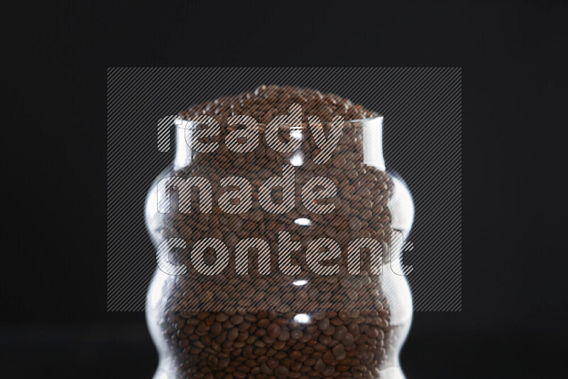 Brown lentils in a glass jar on black background
