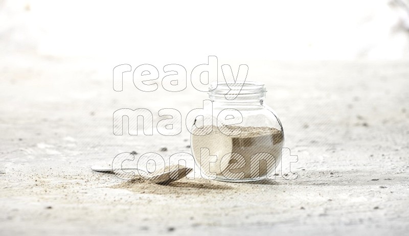 Herbal Glass jar full of white pepper powder and metal spoon full of powder on textured white flooring