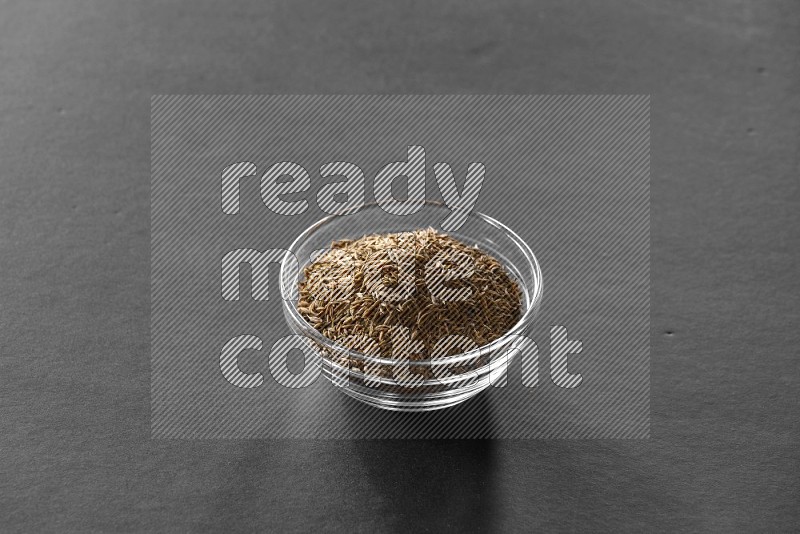 A glass bowl full of cumin on black flooring